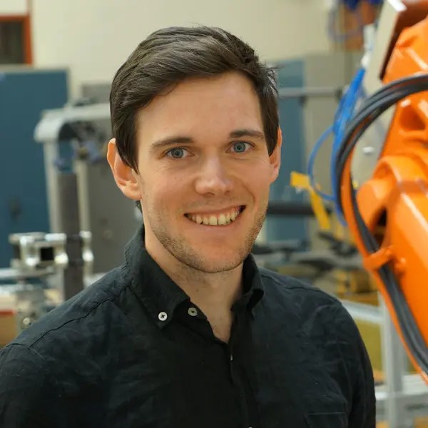 Jon Bokrantz standing beside an orange robot arm