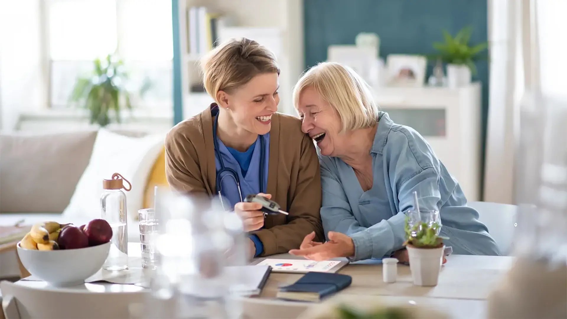 Kvinnlig vårdpersonal och vårdtagare i hemmiljö skrattar tillsammans